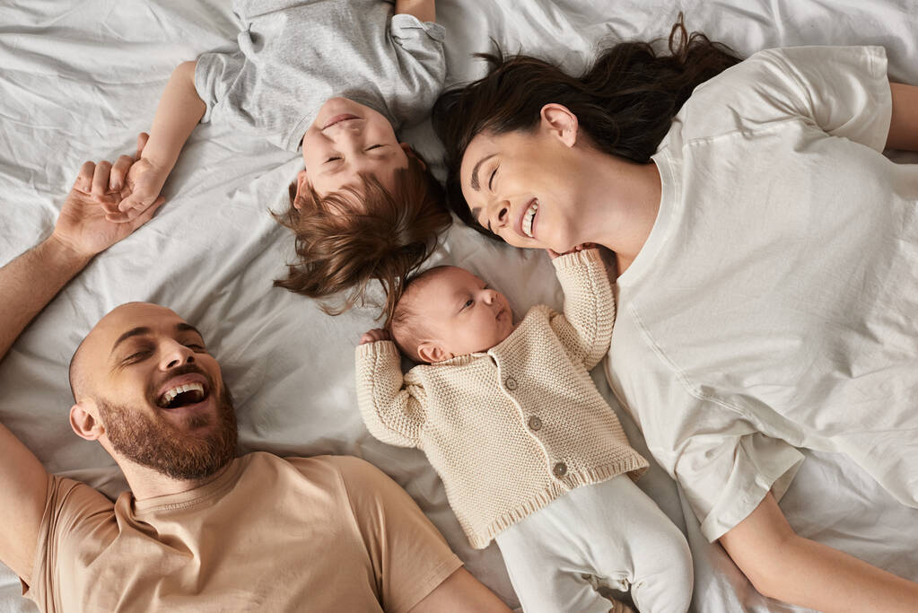 Draufsicht auf glücklich entspannte Familie in gemütlicher Hausmannskleidung, die zusammen im Bett liegt, moderne Elternschaft - Foto, Bild