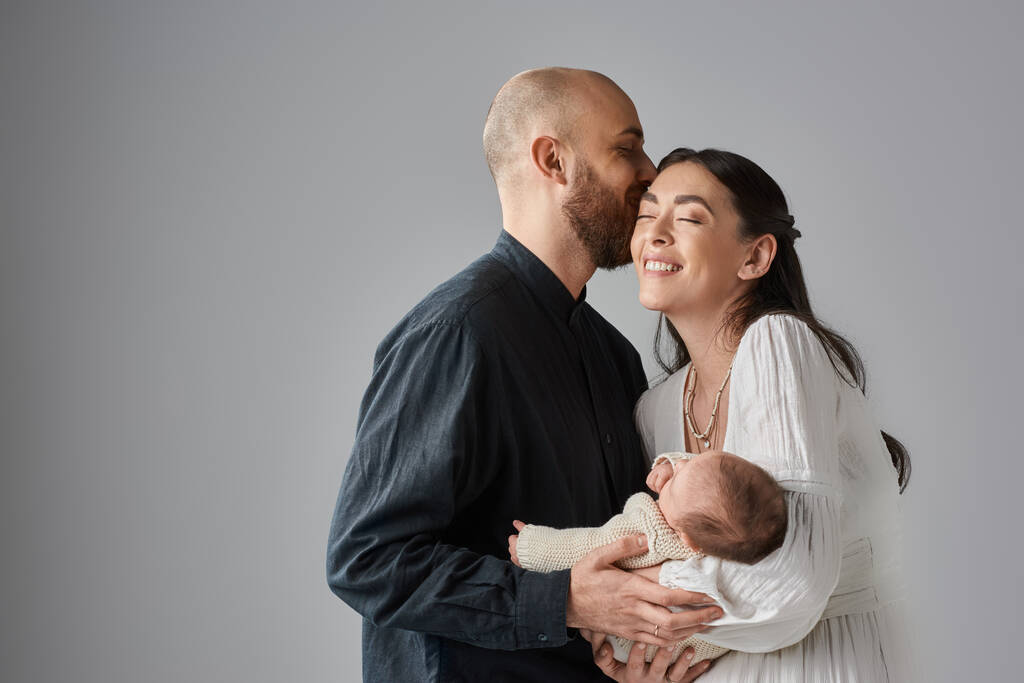 mosolygós gyönyörű anya kezében újszülött baba, míg a férje megcsókolta a homlokát, családi koncepció - Fotó, kép