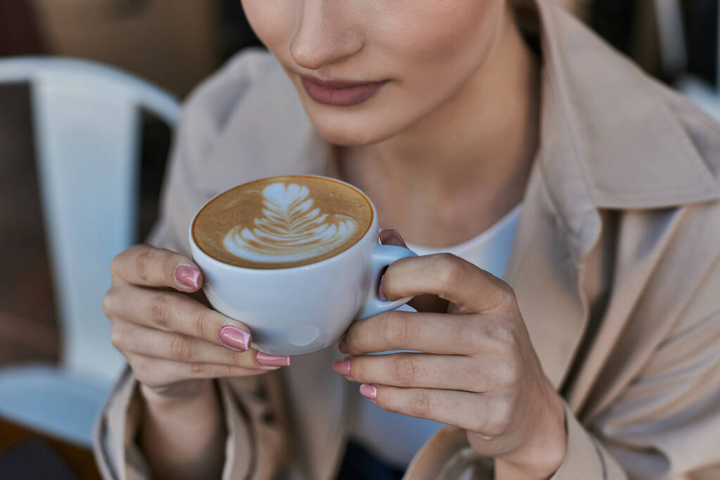 kivágott kilátás nő ballonkabát élvezi a csésze cappuccino kávézóban, nyugodt légkör - Fotó, kép