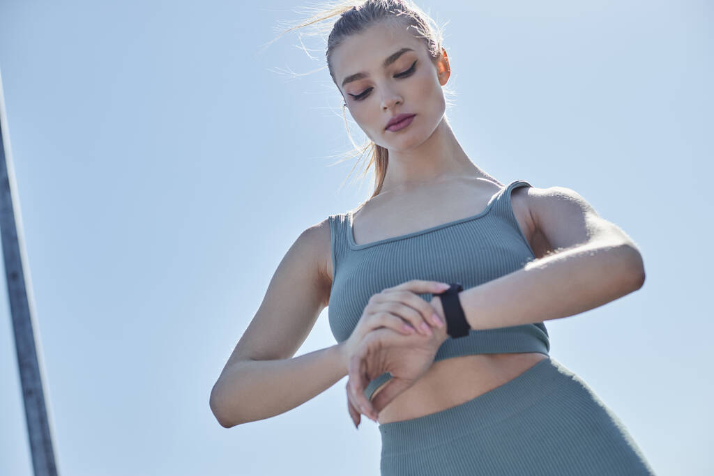 visão de baixo ângulo da jovem mulher em activewear verificando rastreador de fitness no pulso após o treino - Foto, Imagem