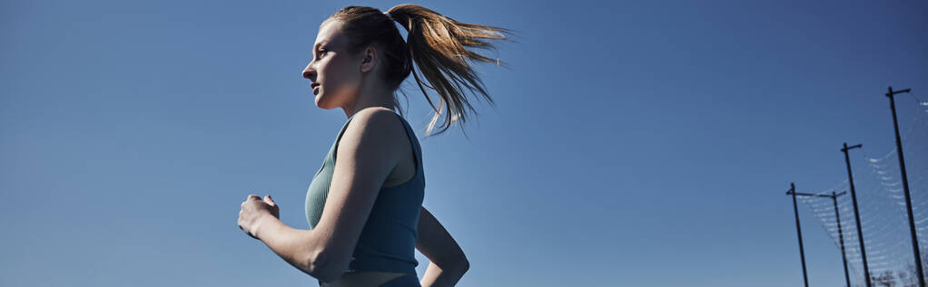 vista lateral de mujer en forma rubia en ropa deportiva corriendo al aire libre, motivación y banner deportivo - Foto, imagen