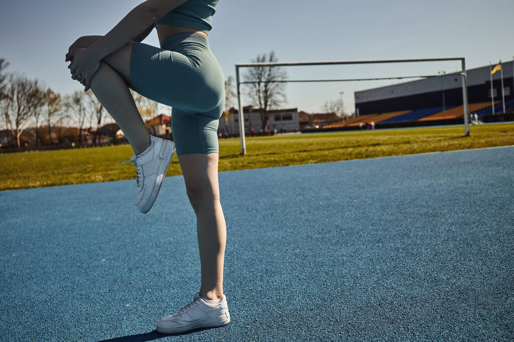Ausgeschnittene Ansicht einer flexiblen Sportlerin, die in enger Aktivkleidung im Freien trainiert, das Bein streckt - Foto, Bild