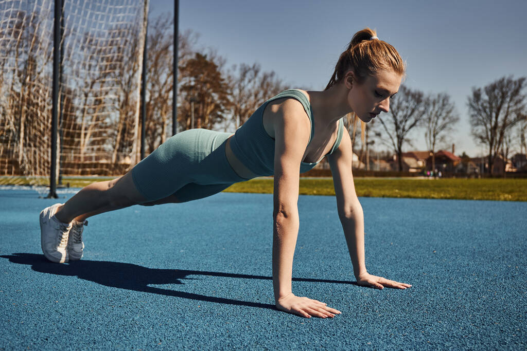 mladá sportovkyně s culíkem cvičení v aktivním oblečení v blízkosti sítě venku, dělá press ups - Fotografie, Obrázek
