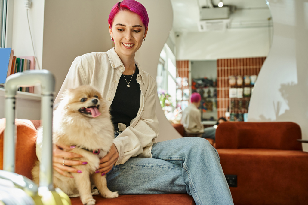 zufriedene Frau sitzt neben Reisetasche im Haustierhotel und kuschelt lustigen Hund, Haustier-Unterkunft - Foto, Bild