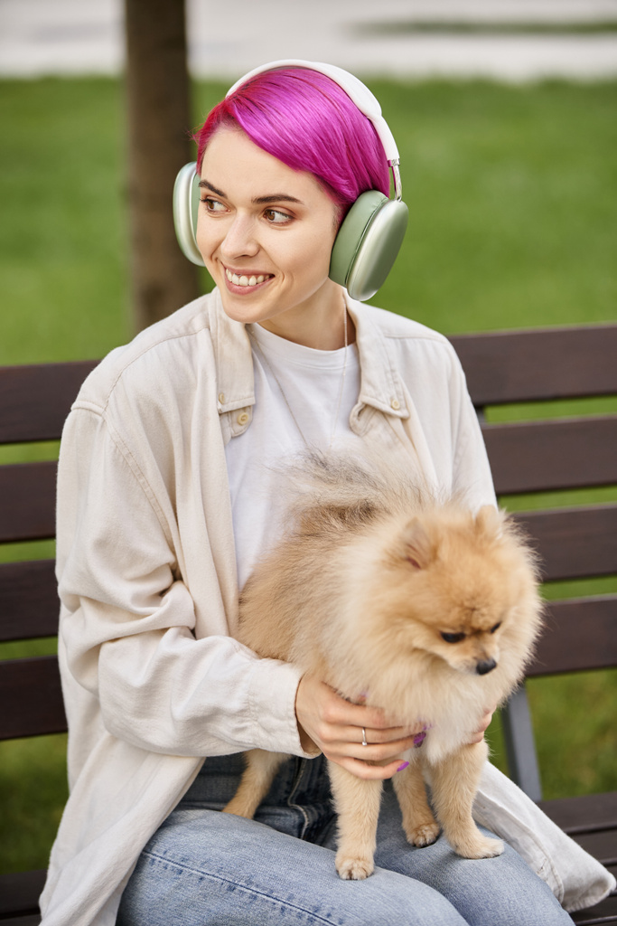 vrolijk vrouw met pomeranian spitz luisteren muziek in hoofdtelefoon en weg te kijken in het park - Foto, afbeelding
