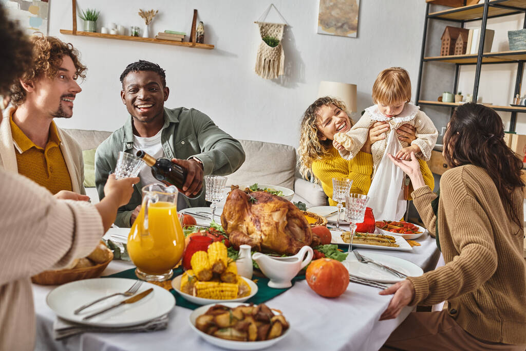 アフリカ系アメリカ人男性がワインをグラスに注ぎ,家庭で感謝祭を祝う多民族家族 - 写真・画像