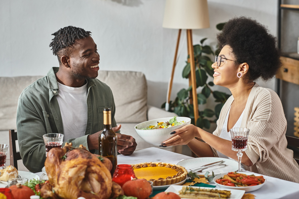 happy african american woman passing bowl with salad to relative during Thanksgiving dinner, turkey - Photo, Image
