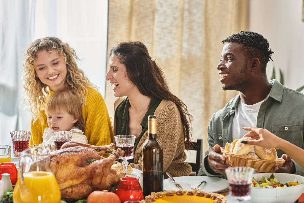 жареная индейка в центре стола, счастливая межрасовая семья празднует День Благодарения вместе - Фото, изображение