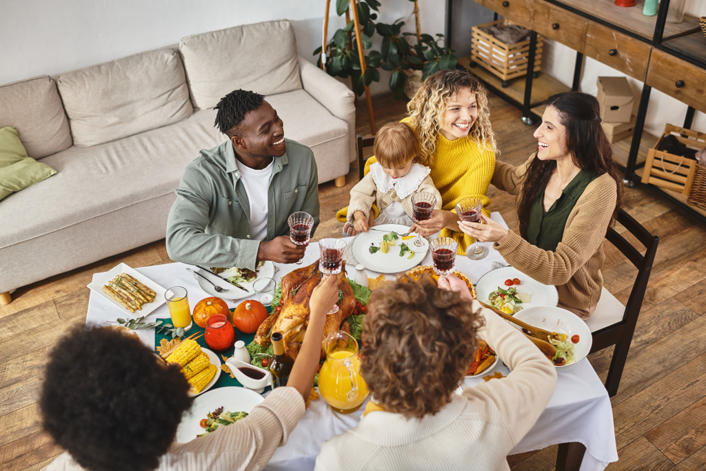 Thanksgiving, glimlachende multi-etnische vrienden en familie juichen glazen wijn in de buurt van kalkoen, bovenaanzicht - Foto, afbeelding