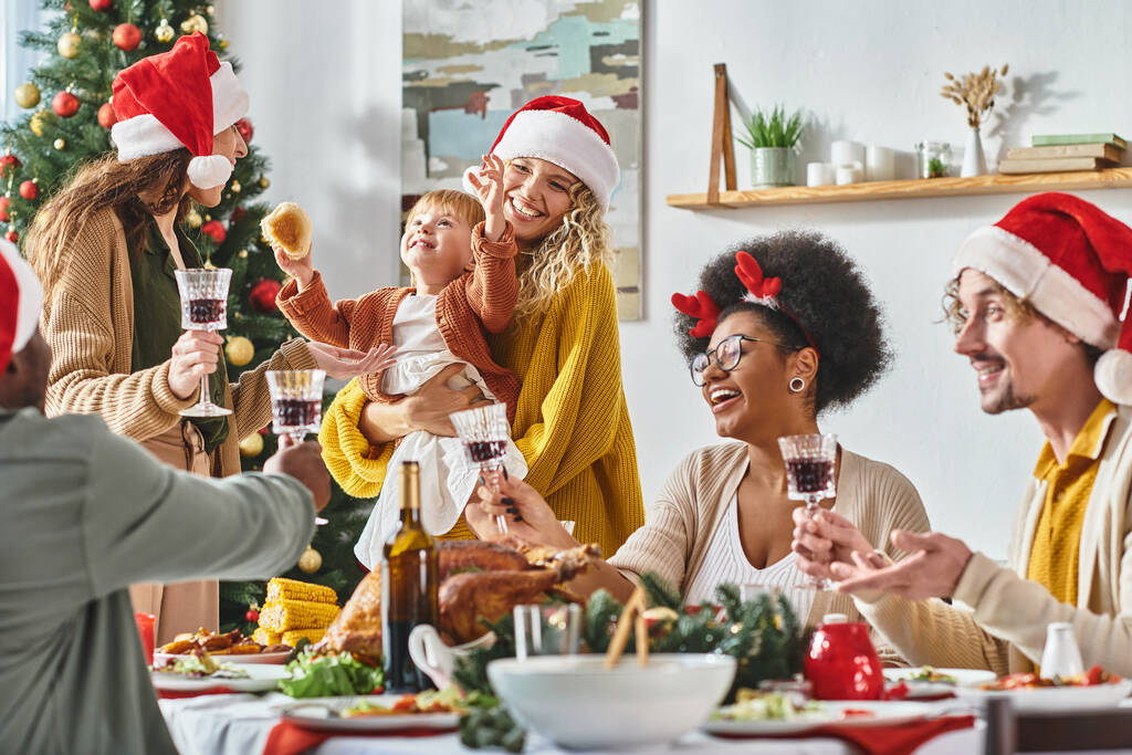 μεγάλη πολυπολιτισμική και χαρούμενη οικογένεια με καπέλα Αϊ-Βασίλη που σφίγγουν τα ποτήρια τους στο Χριστουγεννιάτικο τραπέζι - Φωτογραφία, εικόνα