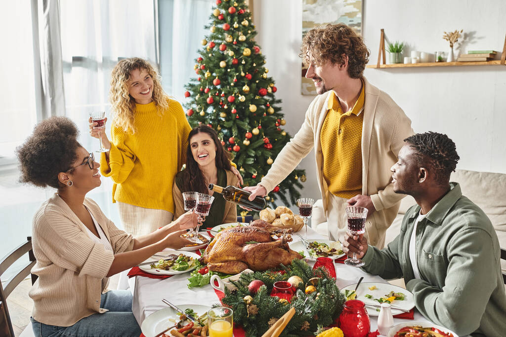große multiethnische Familie in lässigem Outfit genießt Weihnachtsessen und schenkt ein Glas Wein ein - Foto, Bild
