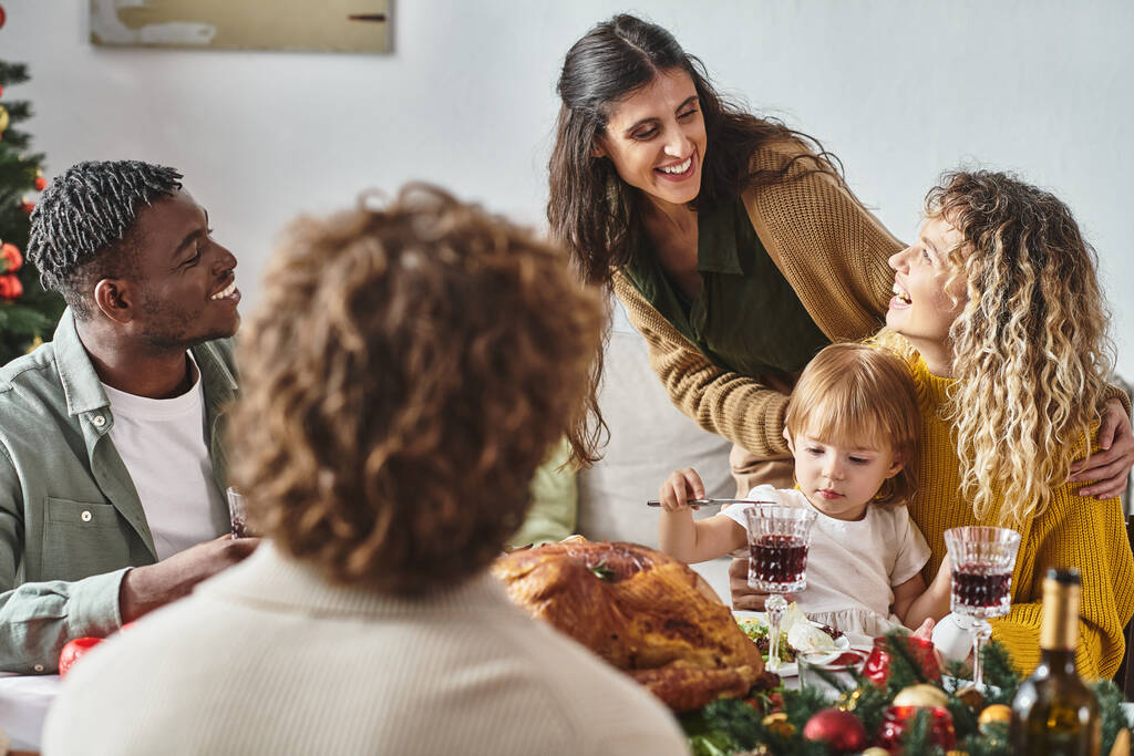 happy multiracial family members sitting at festive table having great time, with daughter in hands - Photo, Image