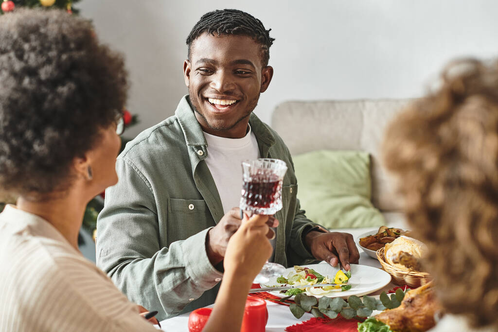 homme afro-américain joyeux assis à la table festive entouré de sa famille, Noël - Photo, image