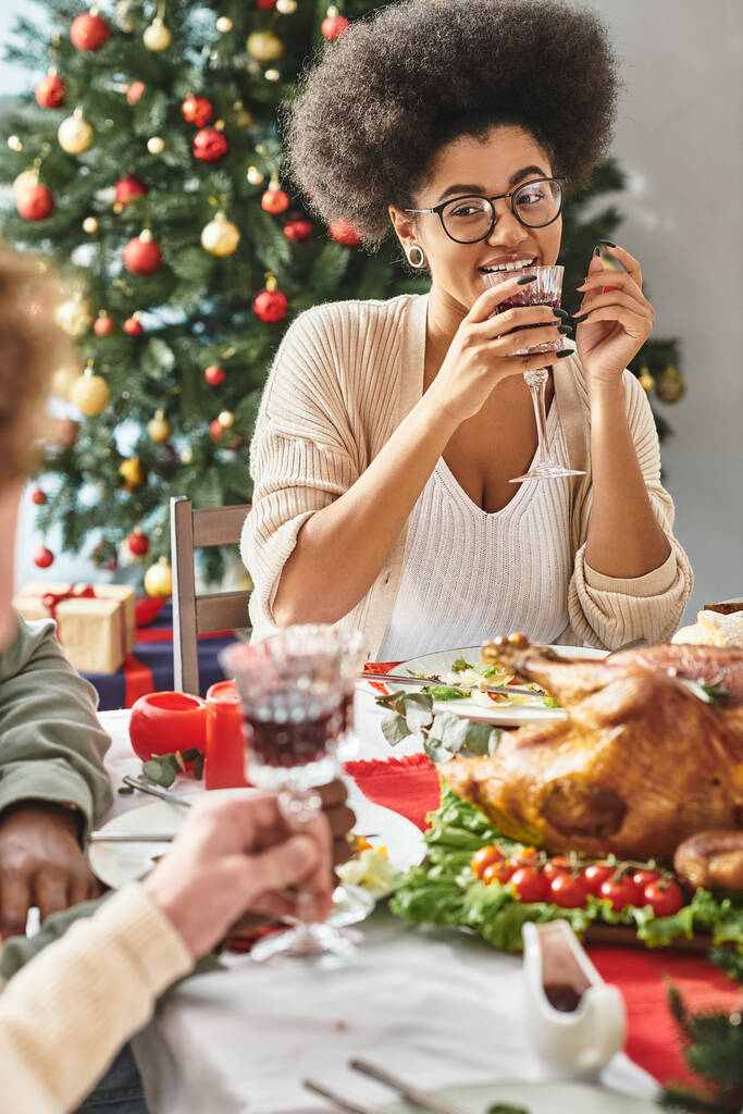 весёлая африканская американка разговаривает со своими родственниками, пьет вино на фоне рождественской елки - Фото, изображение