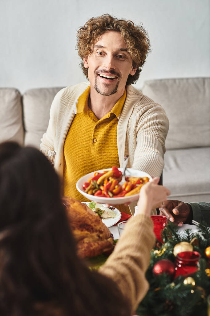 веселый человек в окружении своей семьи за праздничным обедом наслаждаясь и делясь праздничной едой, Рождество - Фото, изображение