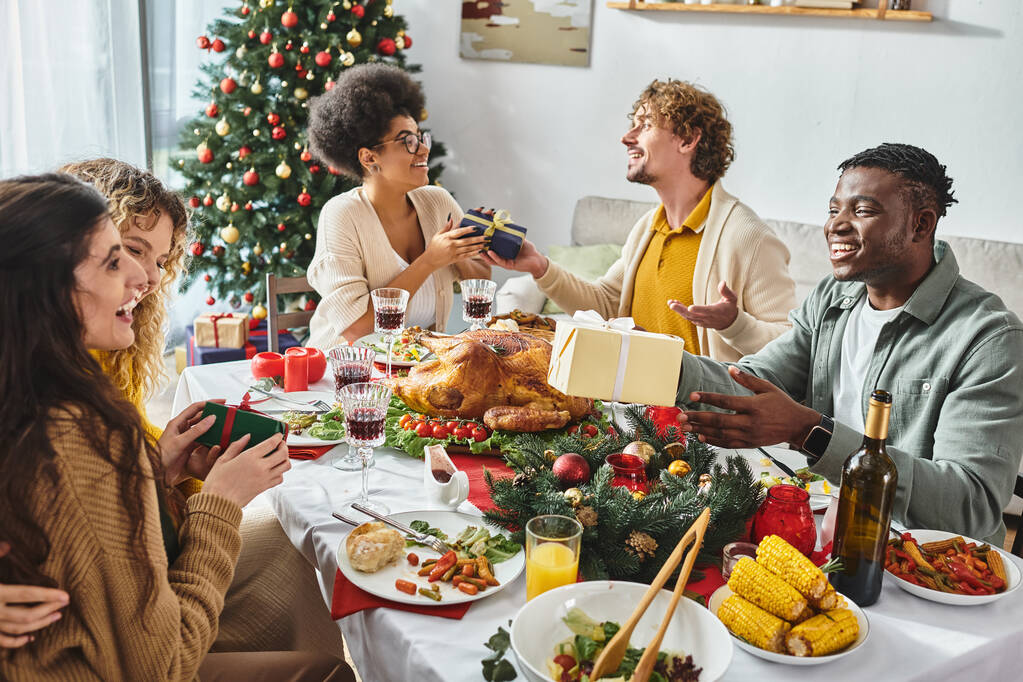 большая веселая и многонациональная семья прекрасно проводит время, празднуя Рождество и обмениваясь подарками - Фото, изображение