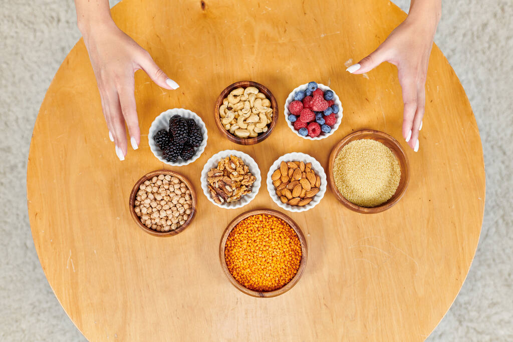 bovenaanzicht van vrouwelijke handen over tafel met assortiment plantaardig vegetarisch voedsel op tafel thuis - Foto, afbeelding