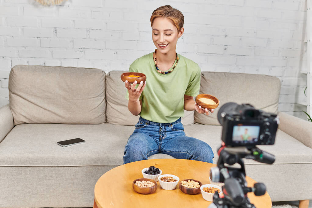 mulher feliz com tigelas de cuscuz e lentilhas perto de câmera digital e vários alimentos à base de plantas - Foto, Imagem