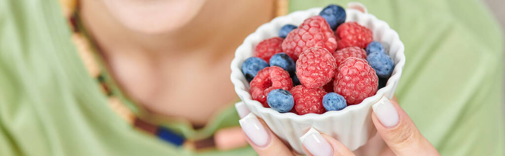 close up view of ripe blueberries and raspberries in hand of blurred vegetarian woman, banner - Photo, Image