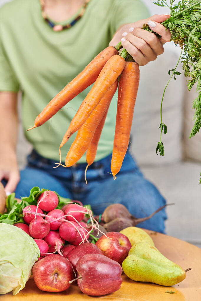 partial view of woman with bunch of carrots near radish and apples with pears, plant-powered diet - Photo, Image