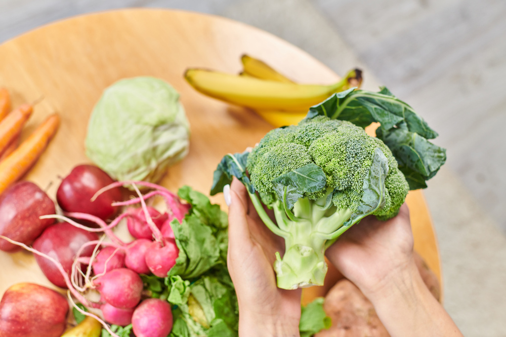テーブル上の野菜や果物の上に新鮮なブロッコリーと女性の手のトップビュー,植物ベースの食事 - 写真・画像