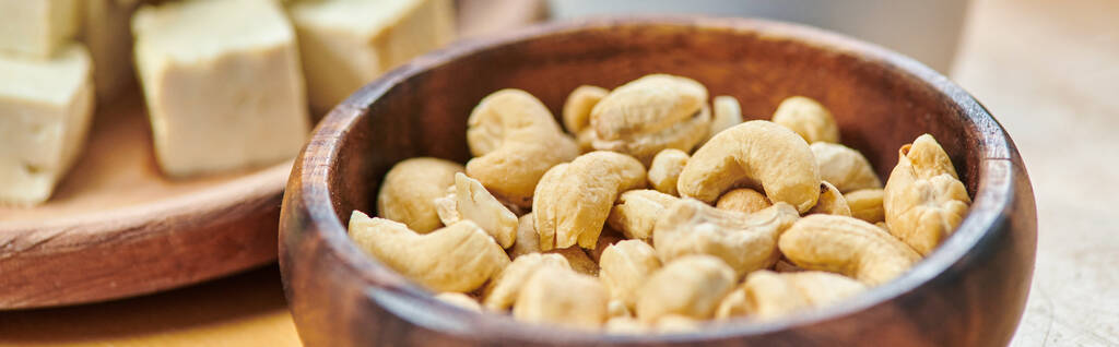 lähikuva puinen kulho cashewpähkinöitä lähellä kuutioiksi tofu juusto, kasvipohjainen ateria käsite, banneri - Valokuva, kuva