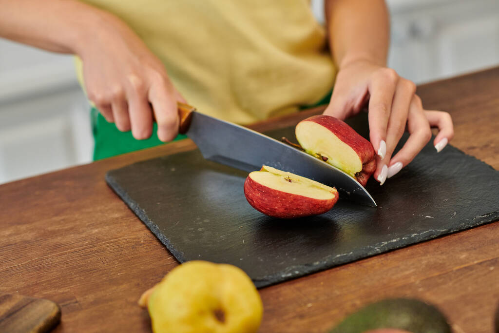 partial view of woman cutting ripe apple on chopping board near pear, vegetarian meal preparation - Photo, Image