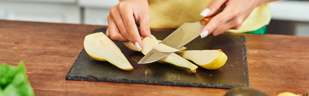 vista ritagliata di donna vegetariana taglio pera matura sul tagliere in cucina, banner orizzontale - Foto, immagini