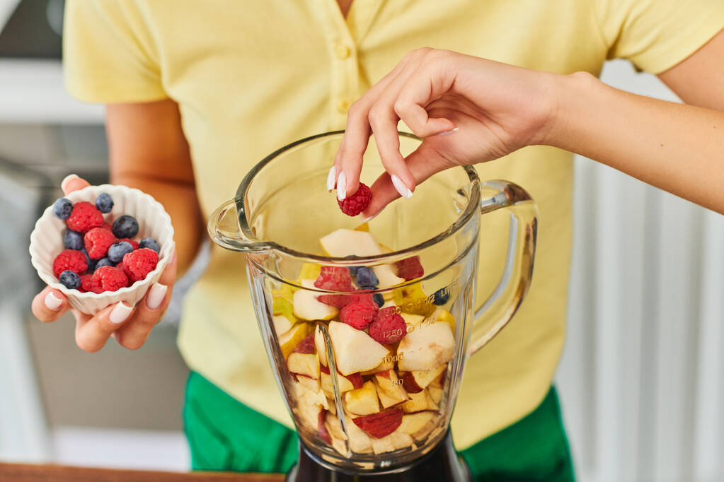 mujer recortada añadiendo frambuesas y arándanos en la licuadora con frutas picadas, dieta vegetariana - Foto, imagen