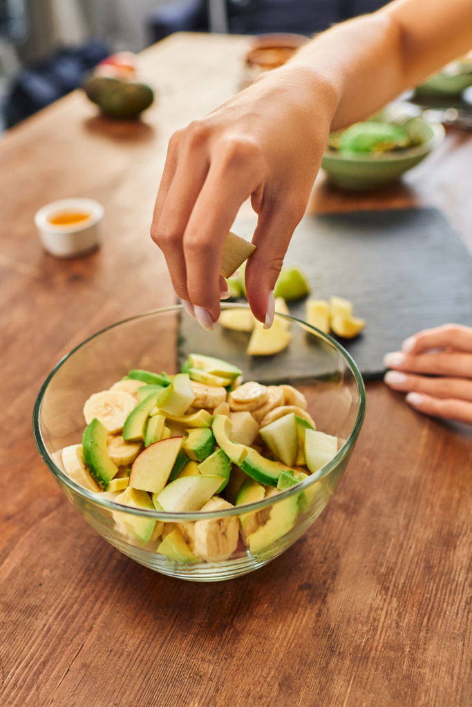 частковий вигляд жінки біля миски зі свіжими подрібненими фруктами, смачний рецепт вегетаріанського салату - Фото, зображення