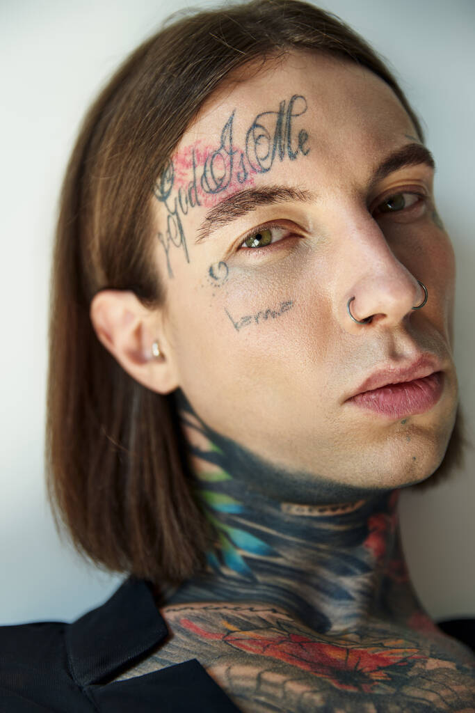 retrato de sexy bonito homem com tatuagens em seu rosto olhando para a câmera no fundo cinza, moda - Foto, Imagem