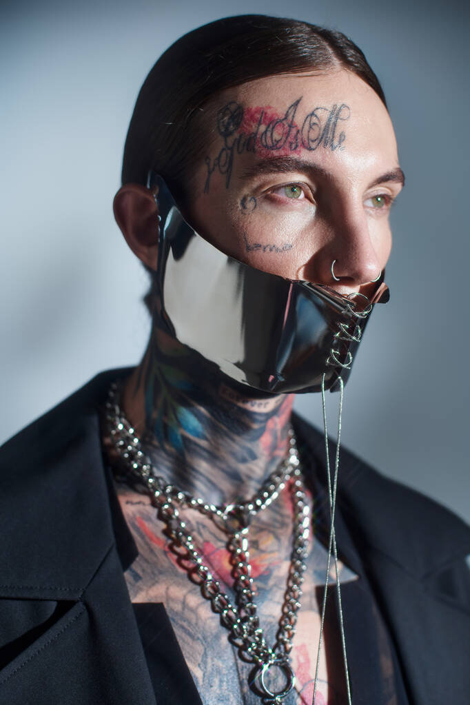 портрет сексуального молодого чоловіка з татуюваннями на обличчі з мереживною маскою та аксесуарами, що дивляться - Фото, зображення