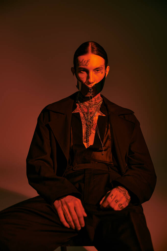 guapo modelo masculino con estilo en traje negro con máscara atada sentado y mirando a la cámara, la moda - Foto, imagen