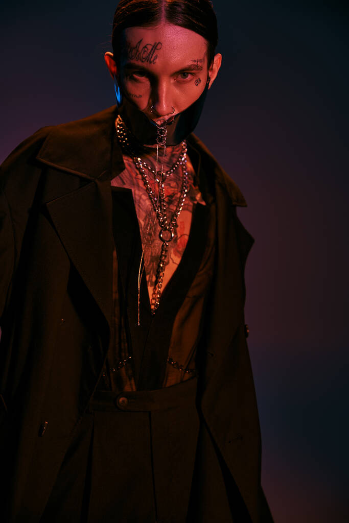 красивый молодой человек с татуировками в черной футуристической одежде, смотрящий в камеру, концепция моды - Фото, изображение
