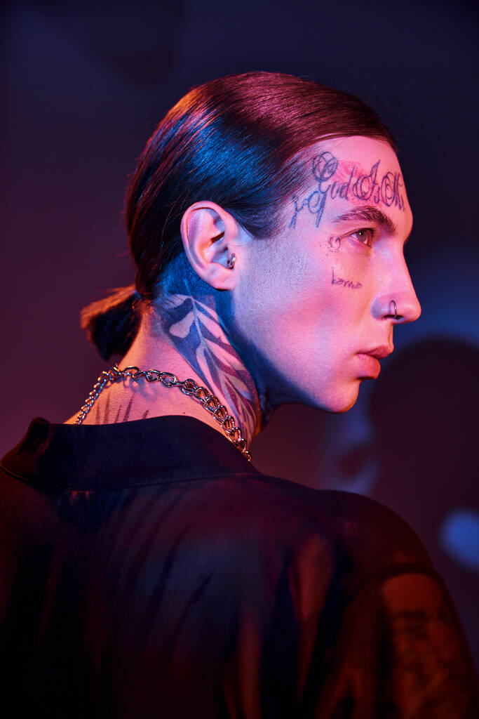 портрет сексуального молодого чоловіка з татуюваннями позує в профіль зі світлом на обличчі, концепція моди - Фото, зображення