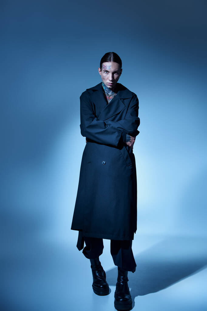 tiro vertical de hombre joven y elegante con tatuajes en elegante abrigo negro mirando a la cámara, la moda - Foto, Imagen