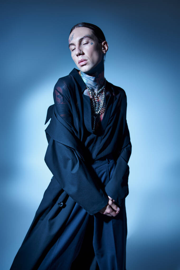 függőleges lövés elegáns fiatalember tetoválás csukott szemmel fekete kabátban, divat koncepció - Fotó, kép