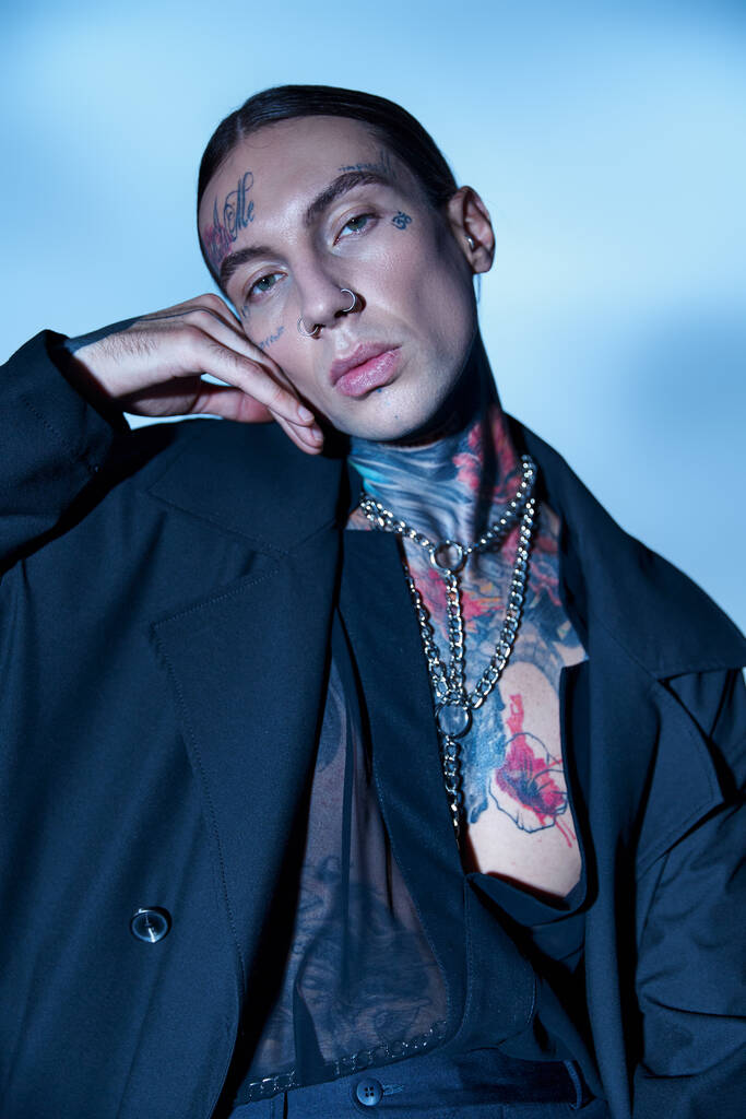 retrato de seductor hombre voguish con tatuajes y piercing mirando a la cámara con la mano cerca de la cara - Foto, Imagen