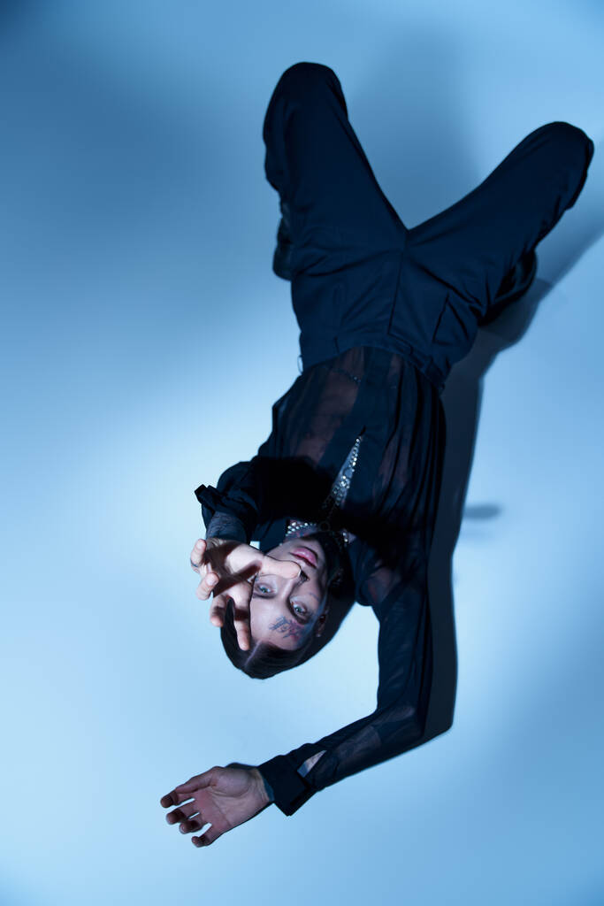 Вид сверху привлекательного стильного мужчины в черном костюме, смотрящего на камеру с рукой перед ней, мода - Фото, изображение