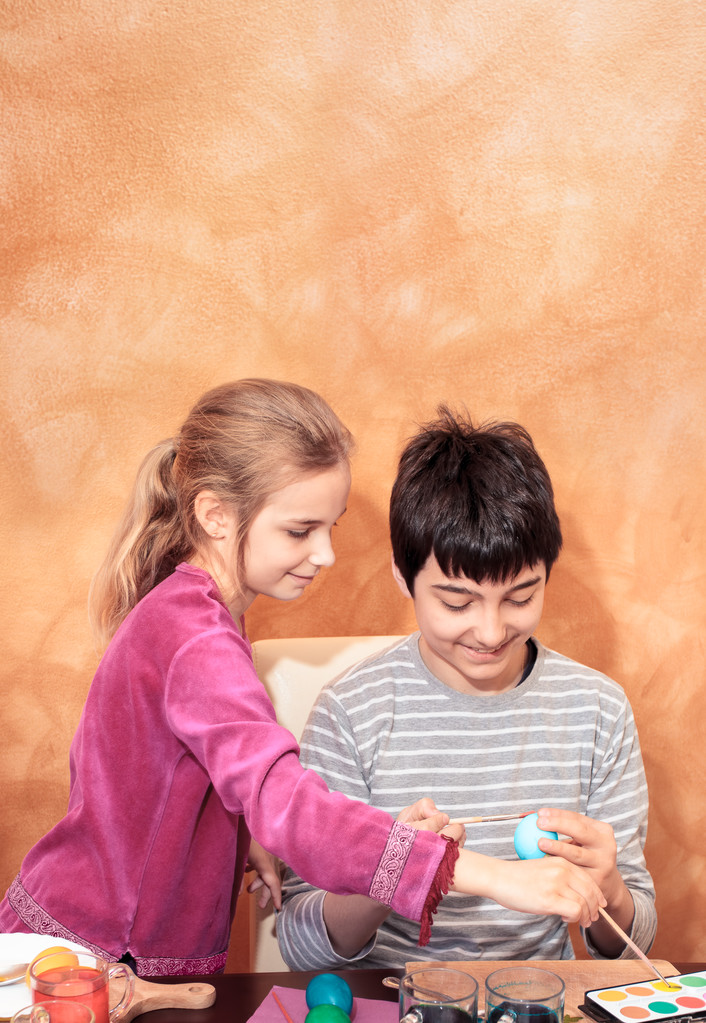 Брат и сестра рисуют пасхальные яйца за столом
 - Фото, изображение