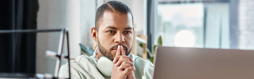вдумчивый человек с наушниками глядя на свой ноутбук с пальцами рядом лицо, рабочий процесс, баннер - Фото, изображение