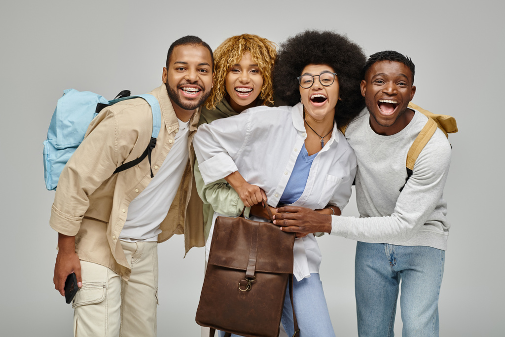 Веселые молодые друзья в повседневных нарядах, улыбающиеся в камеру и держащие рюкзаки, студенческий образ жизни - Фото, изображение