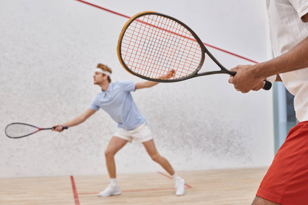 enfoque en el hombre afroamericano en ropa deportiva jugando con pelirroja amigo dentro de la cancha de squash - Foto, Imagen