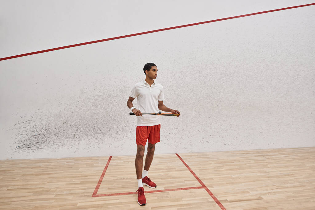 Afrikanischer amerikanischer Sportler hält Squash-Ball und Schläger in der Hand, während er ein Spiel innerhalb des Platzes spielt - Foto, Bild