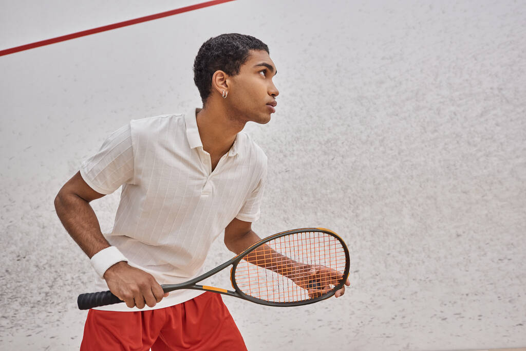 vista lateral, atlético afro-americano homem segurando raquete squash enquanto joga jogo dentro da corte - Foto, Imagem