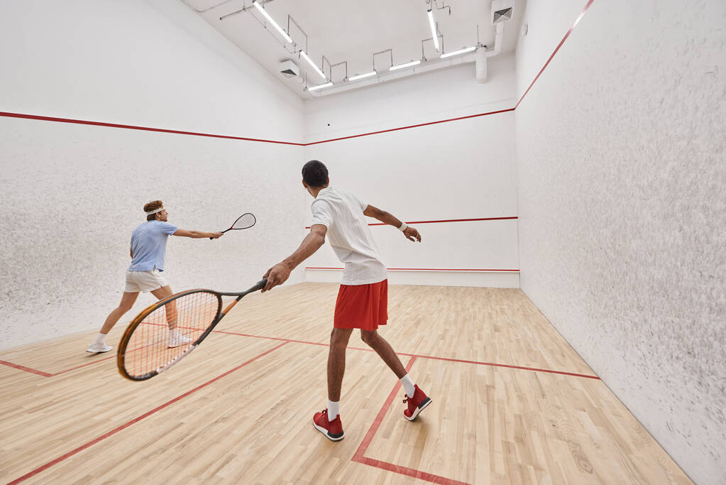 amigos multiculturales en ropa deportiva jugando squash juntos dentro de la corte, estilo de vida activo - Foto, imagen