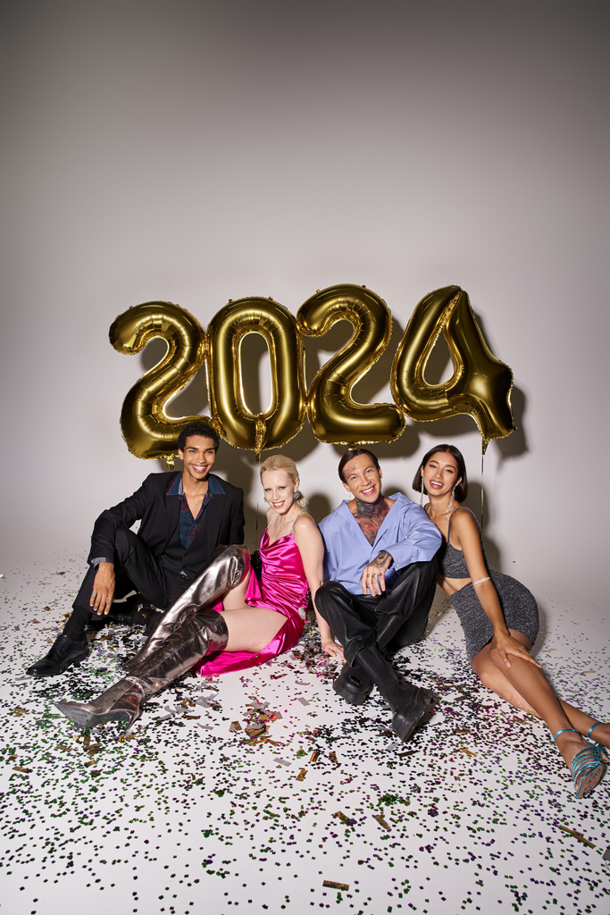 personnes souriantes multiculturelles assis près de confettis et ballons avec des numéros 2024, Bonne année - Photo, image