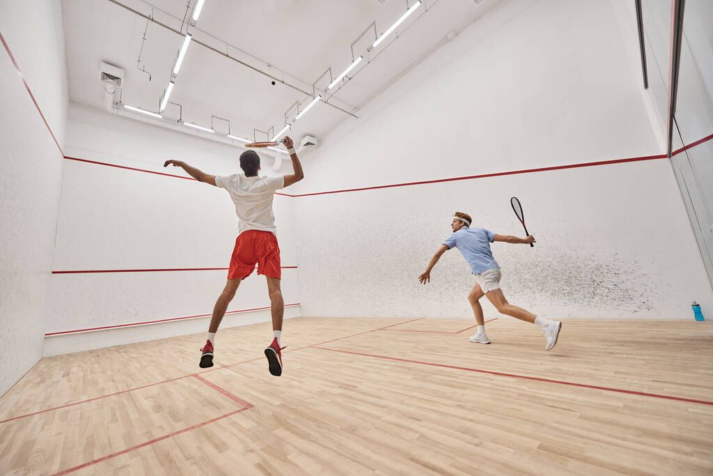 Spor giyim sektöründe genç ve aktif sporcular sarayın içinde squash oynarken atlıyorlar. - Fotoğraf, Görsel