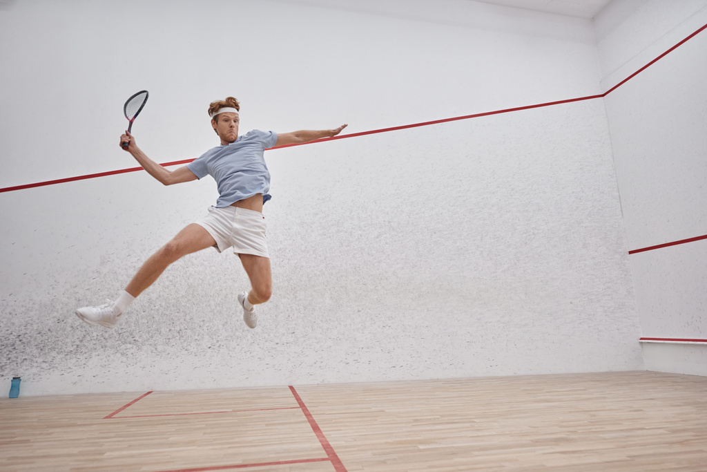 liike laukaus, urheilullinen urheilija tilalla maila ja hyppääminen pelatessaan squash sisällä tuomioistuimessa - Valokuva, kuva