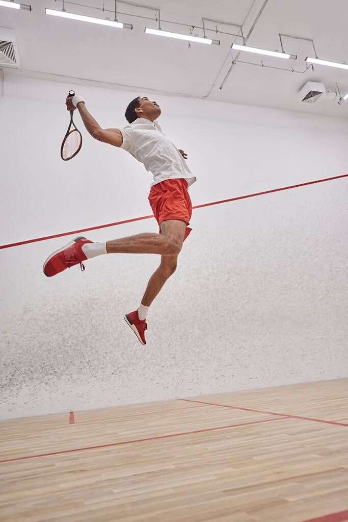 motion shot, motivato giocatore afroamericano che tiene la racchetta mentre salta e gioca a squash - Foto, immagini